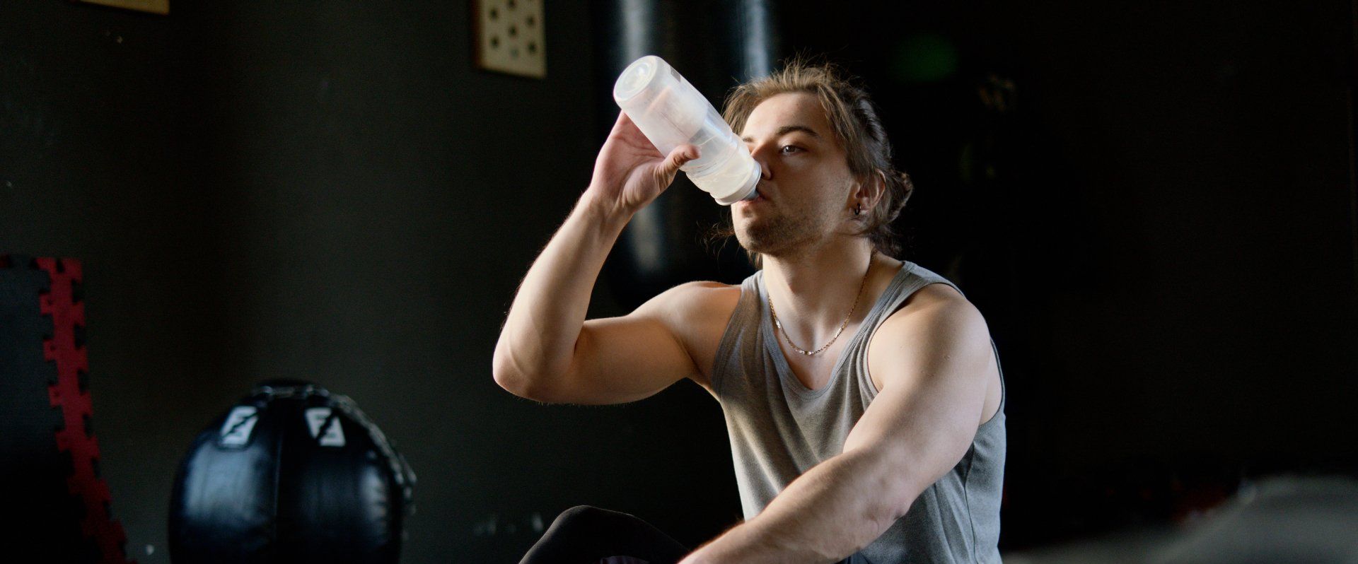 A man is drinking water from a bottle in a gym.