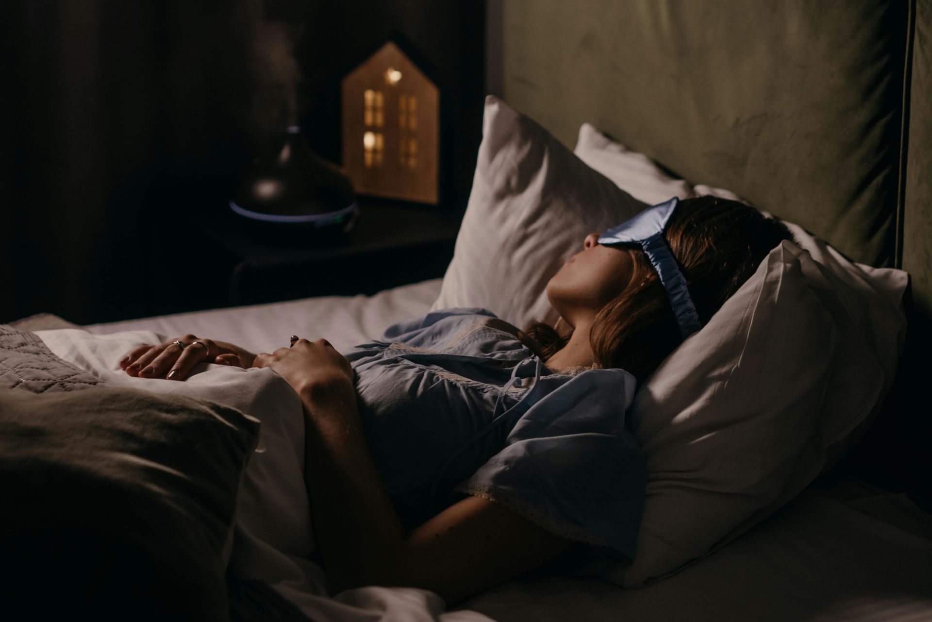 A woman is sleeping in a bed with a sleep mask on her eyes.
