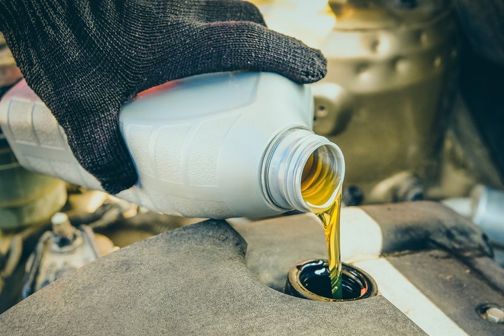 Gloved Hand Pouring Oil From a Bottle — Fischer Automotive in Svensson Heights, QLD