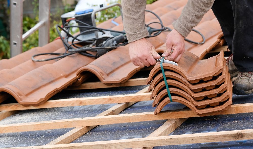 A Man is Stacking Tiles on Top of Each Other on a Roof — RJT Roofing In Tuggeranong, ACT