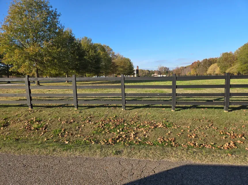 A wooden fence surrounds a grassy field with trees in the background.