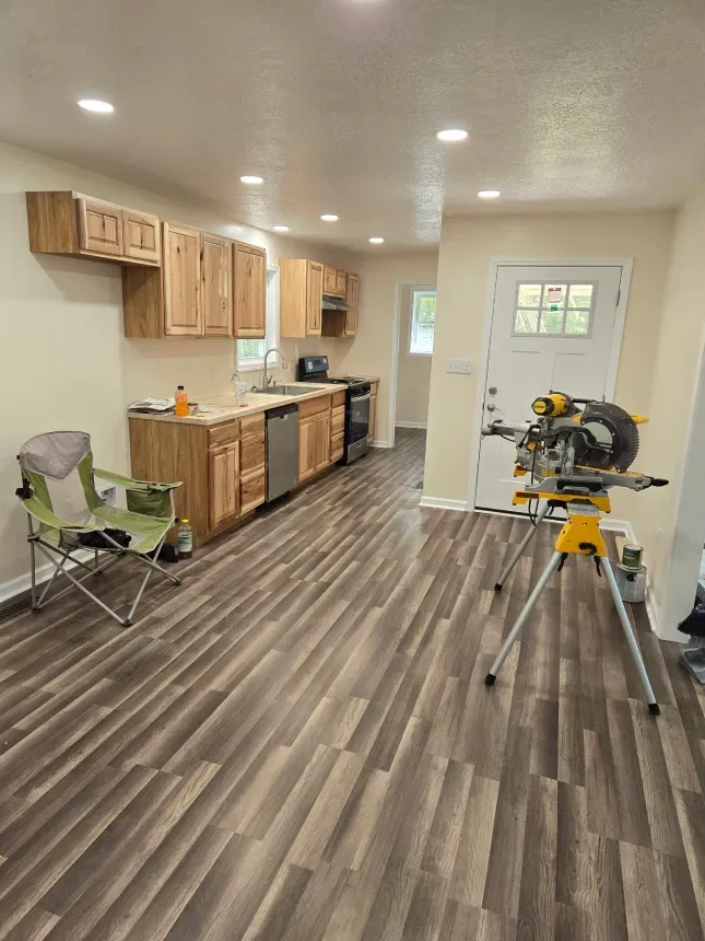 A kitchen with wooden floors , cabinets , a chair and a miter saw.