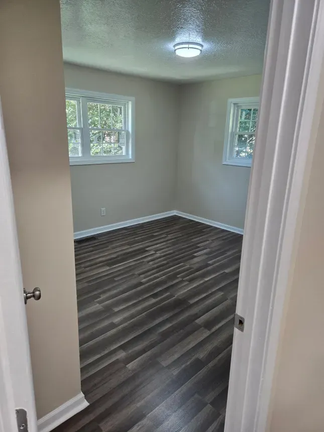 A bedroom with hardwood floors and two windows.