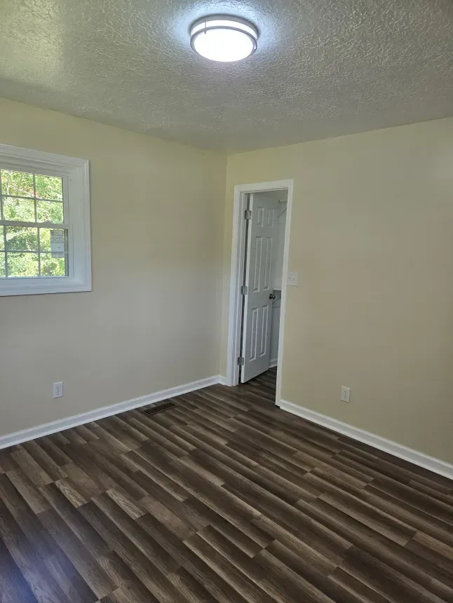 An empty bedroom with hardwood floors and a window.