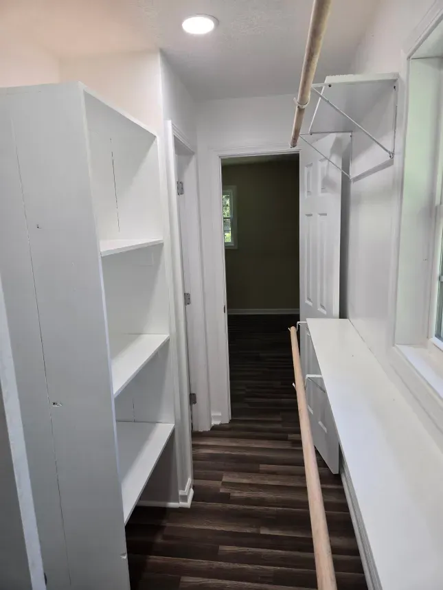 A walk in closet with white shelves and a window.