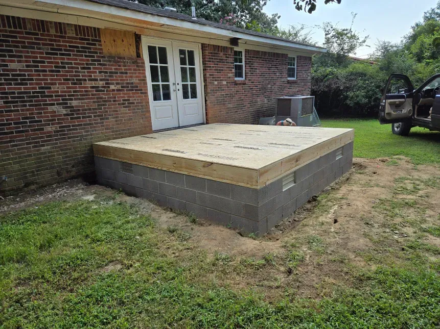 A wooden deck is being built in front of a brick house.