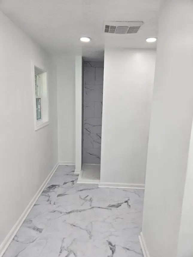 A hallway with marble floors and white walls leading to a bathroom.