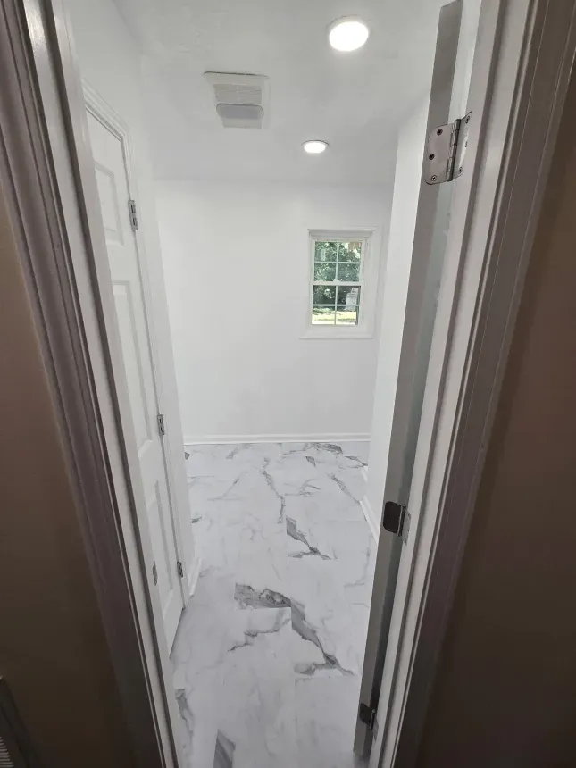 A hallway in a house with marble floors and a window.