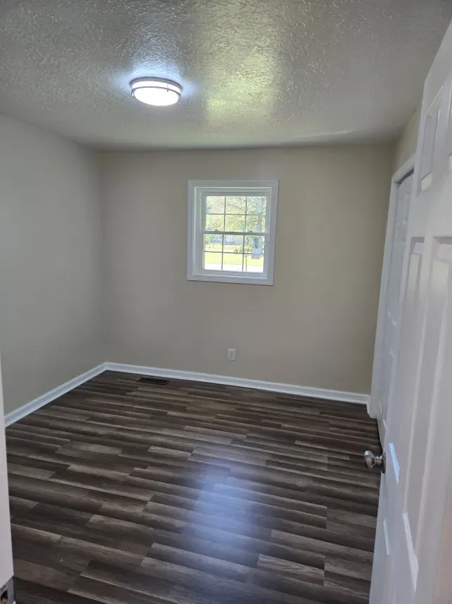 An empty bedroom with hardwood floors and a window.