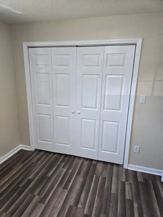 A bedroom with hardwood floors and a closet with white doors.