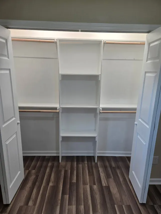 A walk in closet with wooden floors and white shelves.