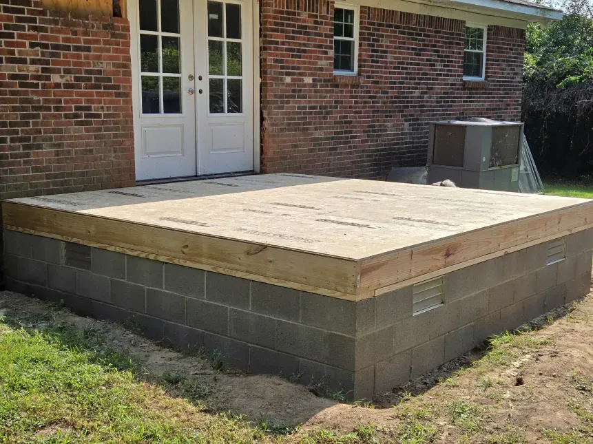 A wooden deck is being built in front of a brick house.