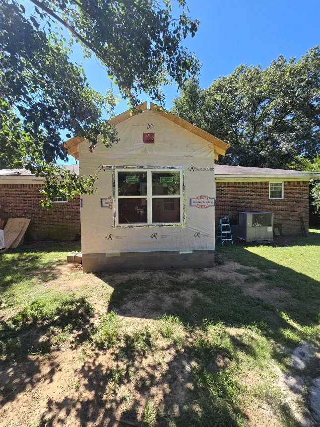 A small house is being built in the backyard of a brick house.