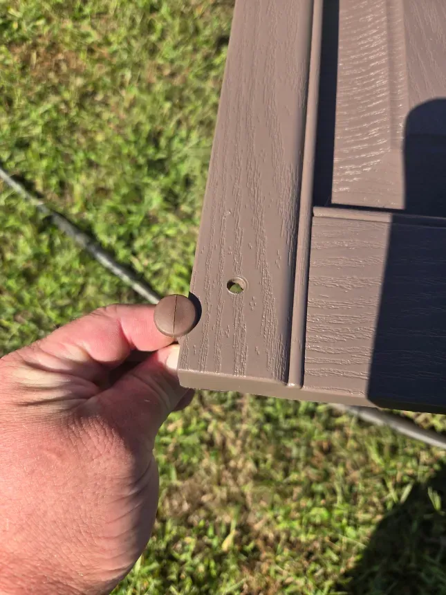A person is holding a piece of wood with a screw in it.