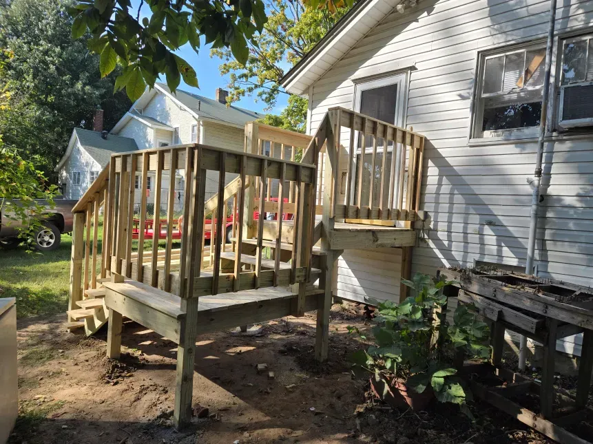 A wooden deck is sitting in front of a white house.