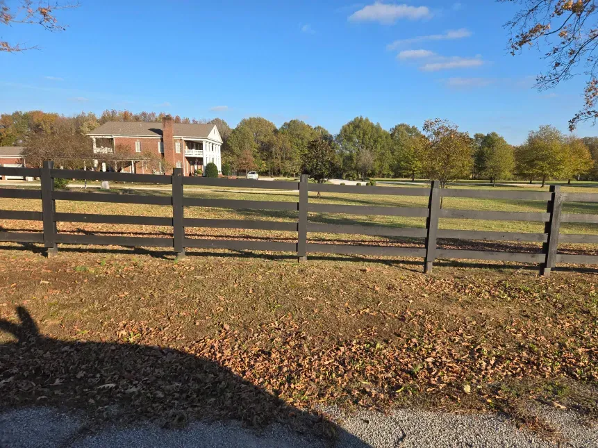 A wooden fence surrounds a grassy field with a house in the background.