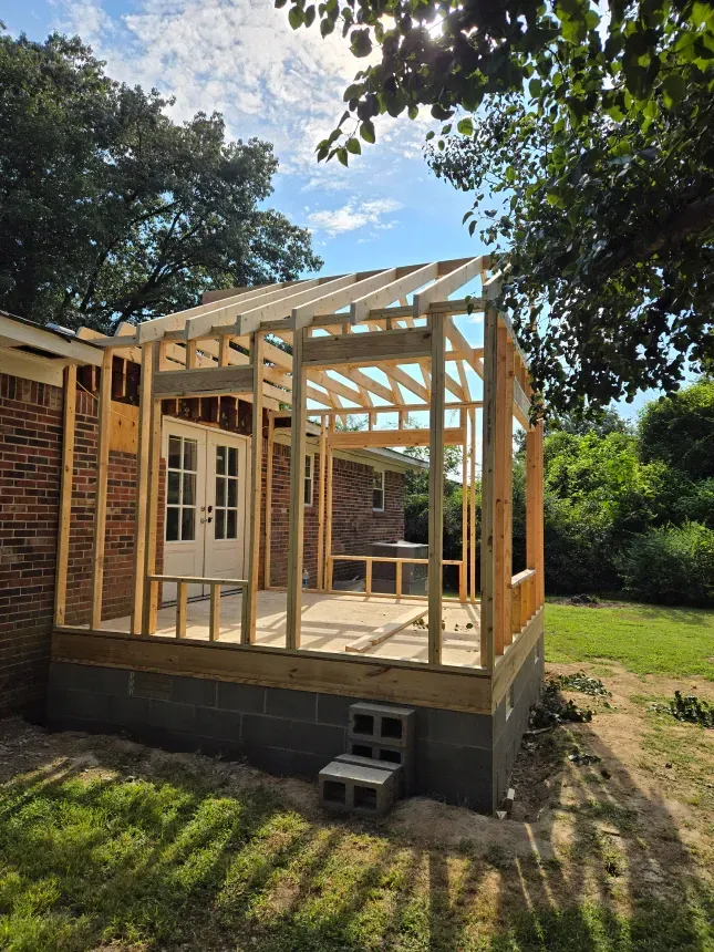 A wooden structure is being built on the side of a brick house.