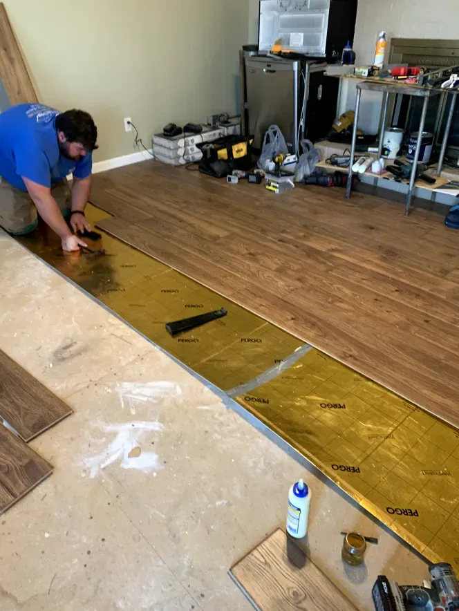 A man is installing a wooden floor in a living room.