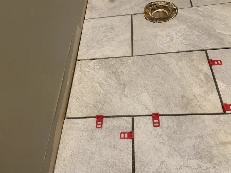 A bathroom floor with tiles and a toilet drain.