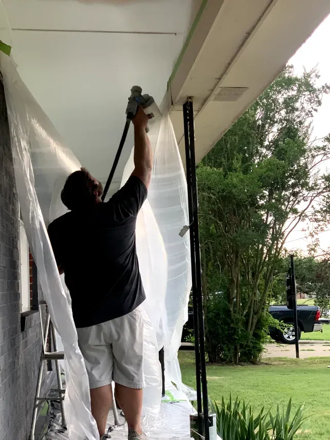 A man is painting the ceiling of a house with a sprayer.