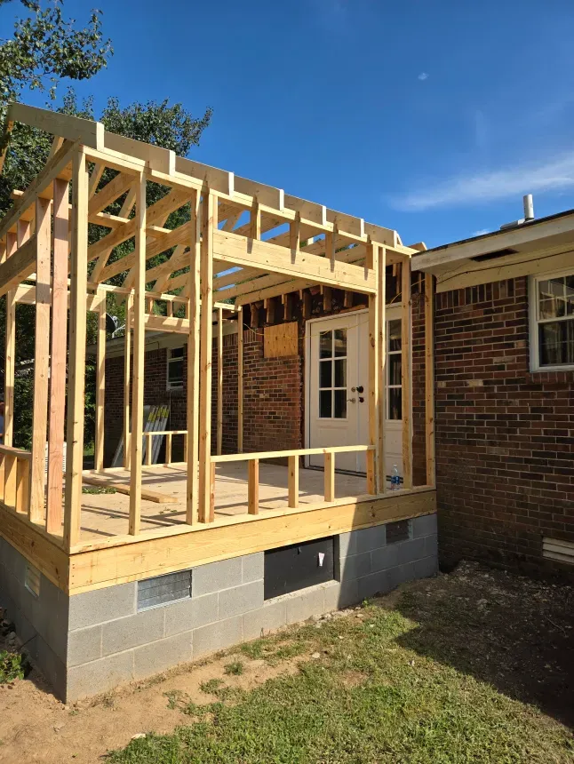 A wooden structure is being built on the side of a brick house.