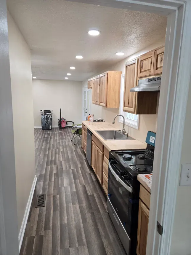A kitchen with a stove , sink , cabinets and hardwood floors.