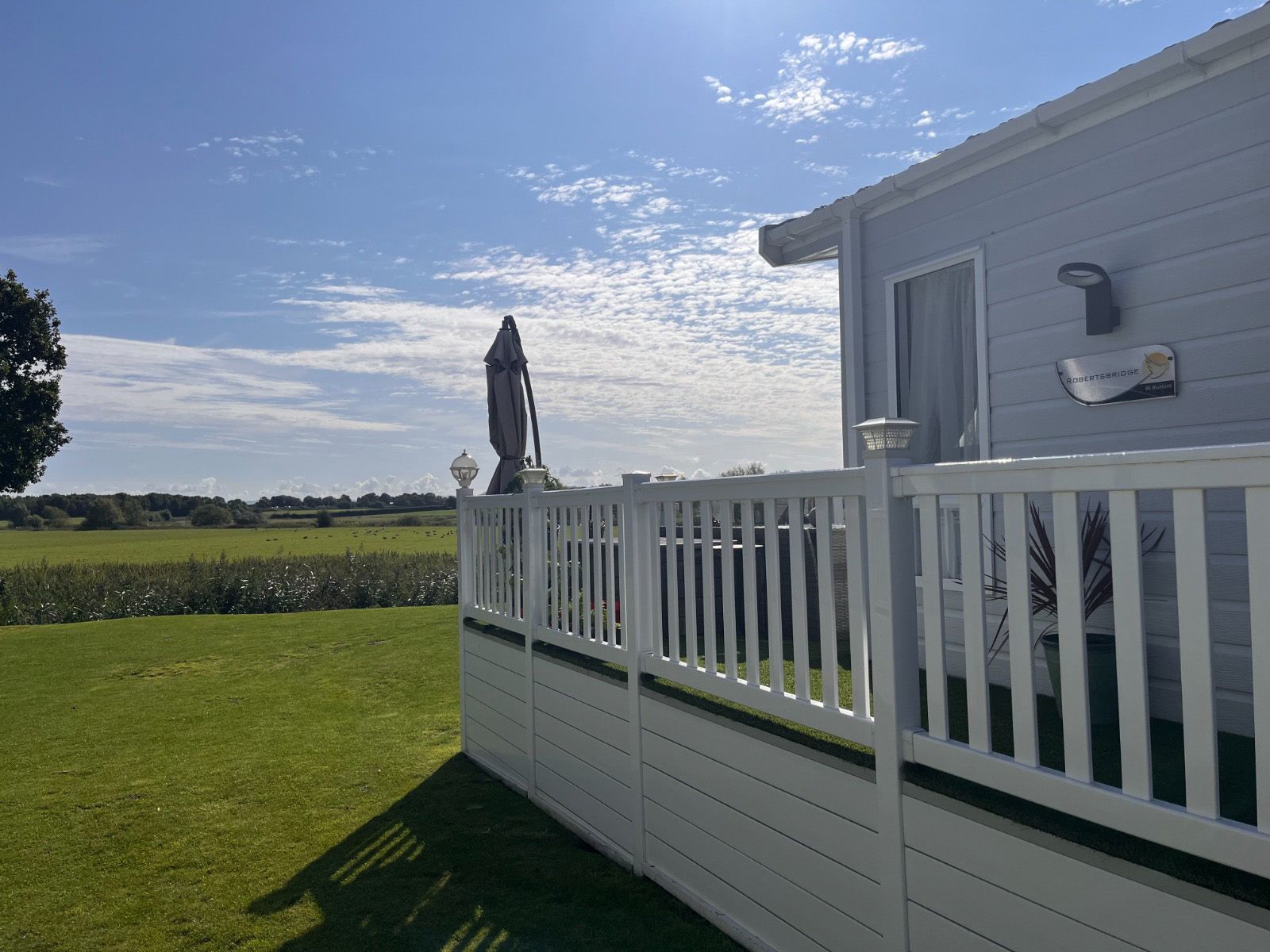 A white fence surrounds a mobile home with a view of a field.