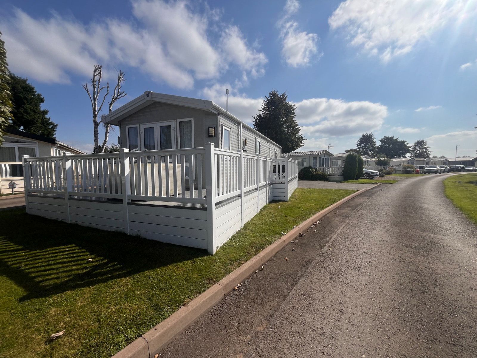 A mobile home with a large deck is sitting on the side of a road.