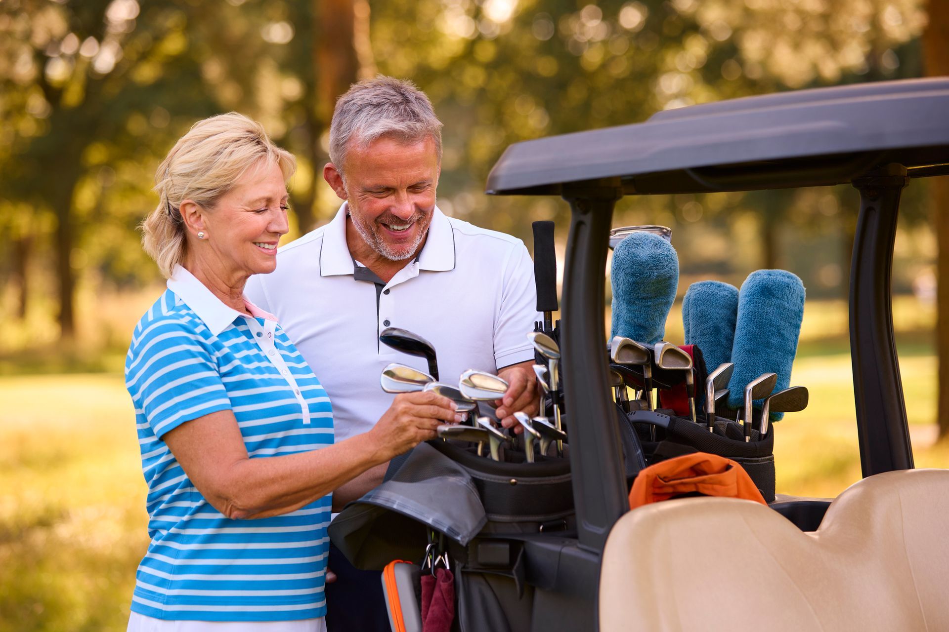 A man and a woman are standing next to a golf cart on a golf course.