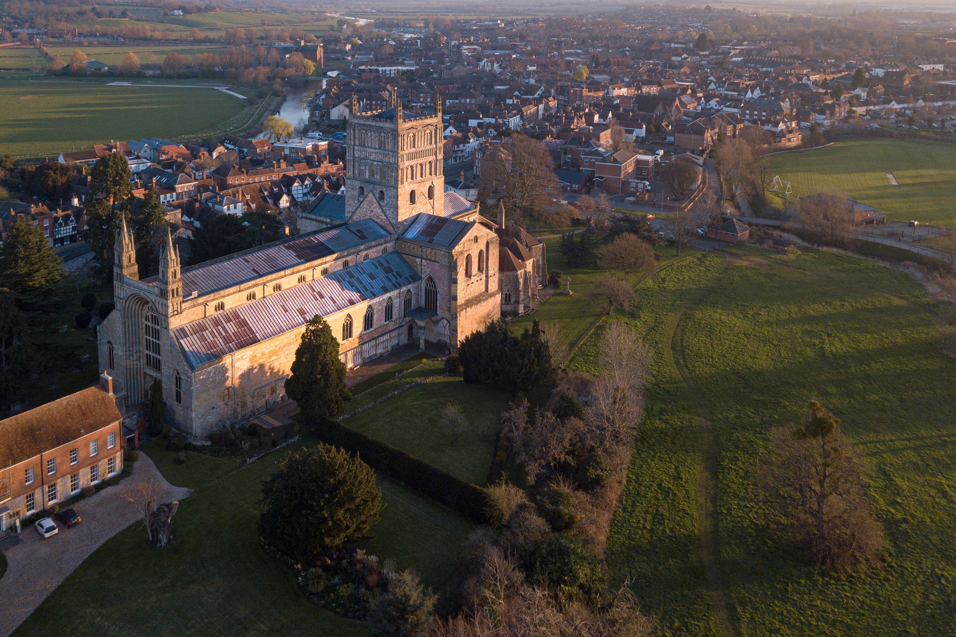 An aerial view of a church in the middle of a field with a city in the background in Tewkesbury