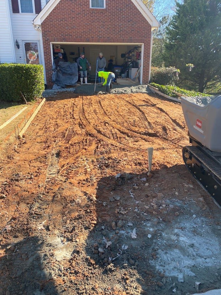A group of people are working on a driveway in front of a brick house.