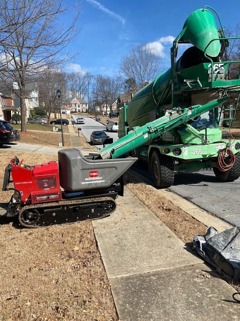 A concrete mixer is pouring concrete on a sidewalk next to a dump truck.