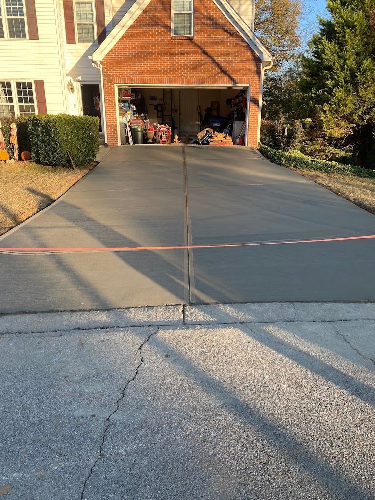 A concrete driveway leading to a brick house with a garage.