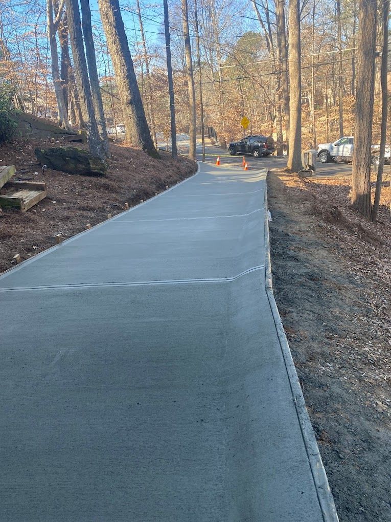 A concrete walkway leading to a parking lot in the woods.