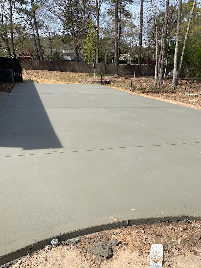 A concrete driveway is being built in a backyard with trees in the background.