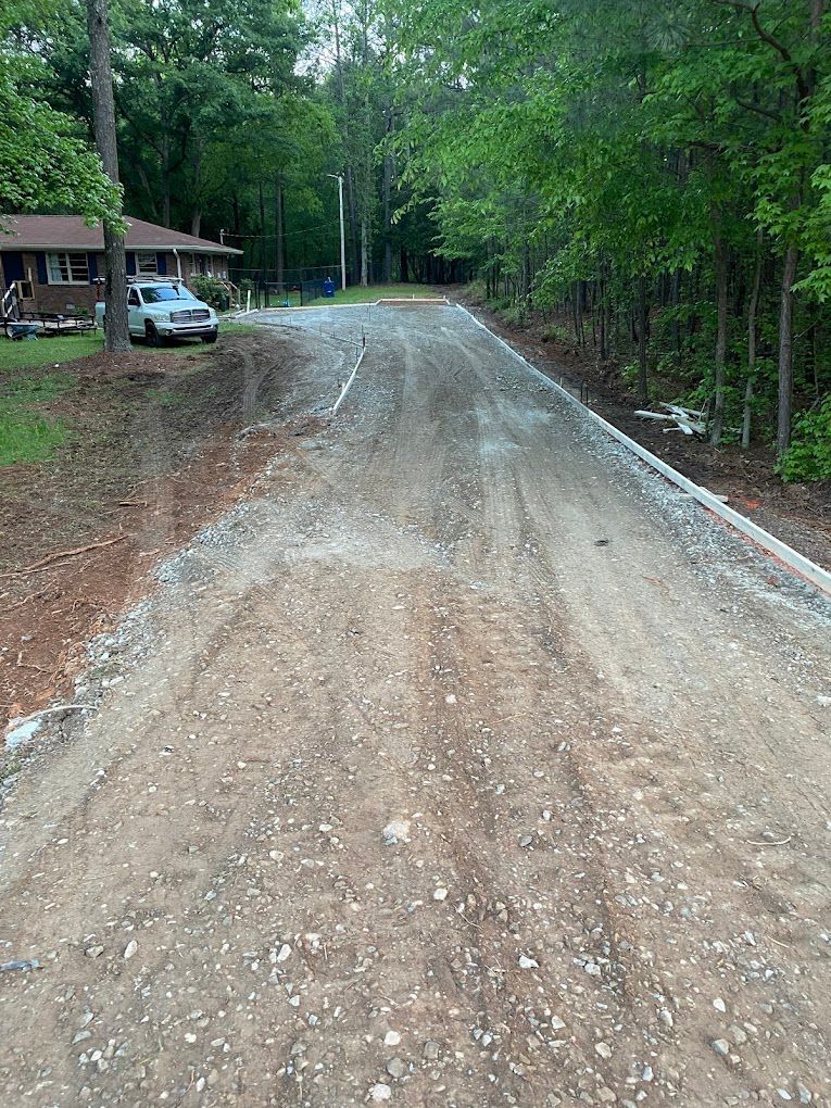 A dirt road with a house in the background and trees on the side.