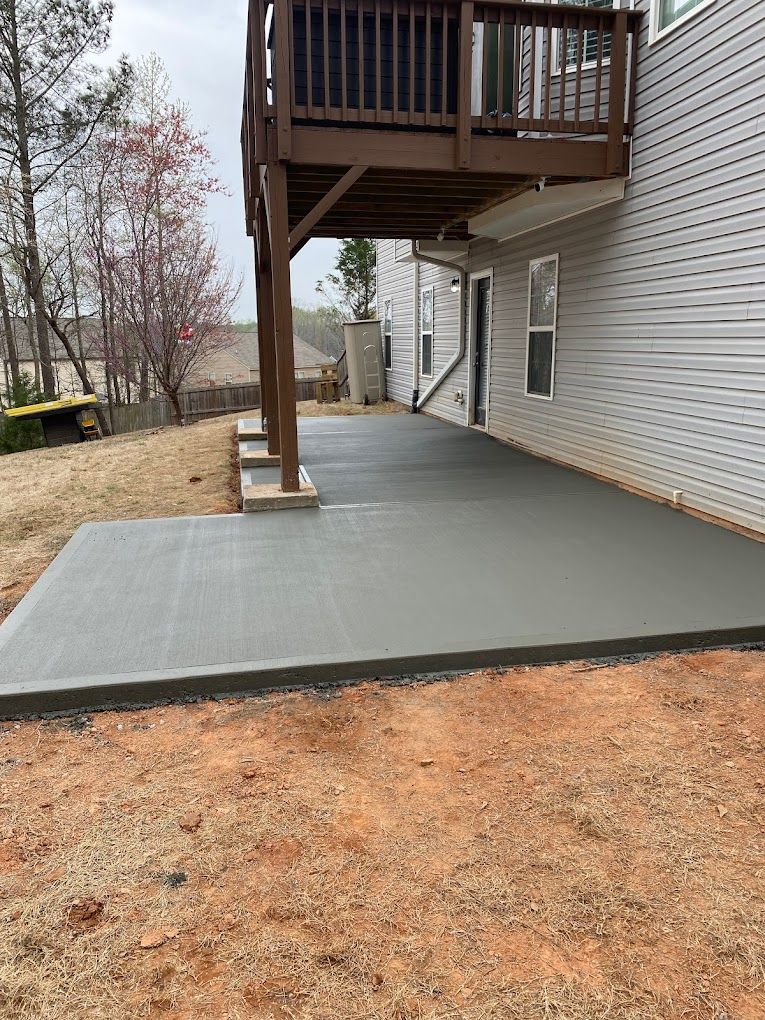 A concrete patio with a deck underneath it in front of a house.