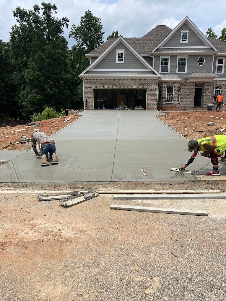 A couple of men are working on a concrete driveway in front of a house.