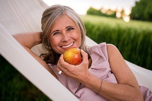 a woman is laying in a hammock holding an apple .