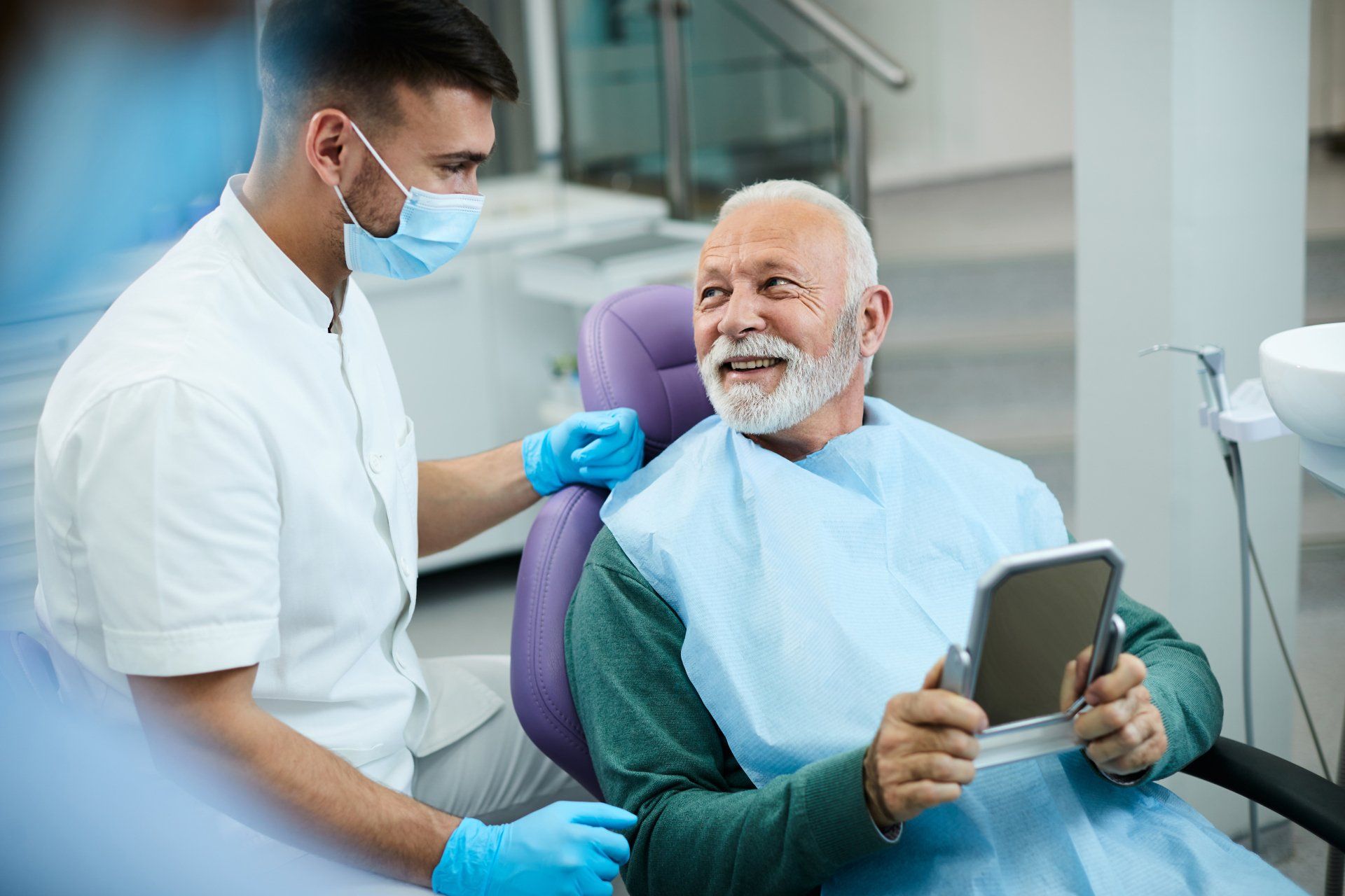 an elderly man is sitting in a dental chair looking at a tablet .