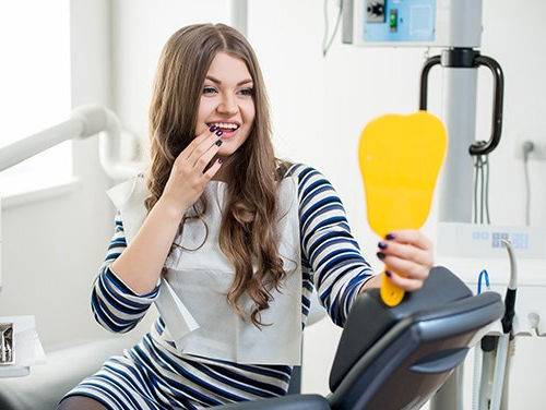a woman is sitting in a dental chair looking at her teeth in a mirror .