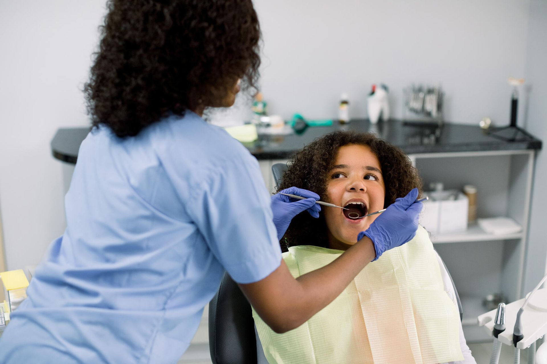 A female dentist is examining a young girl 's teeth in a dental office.