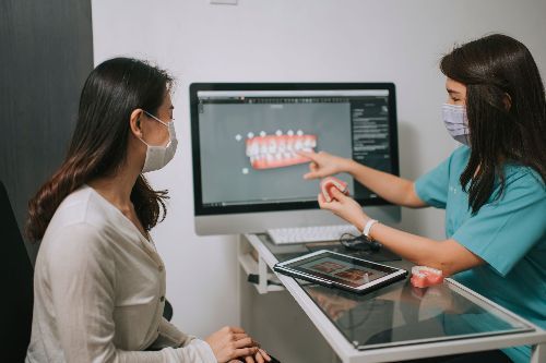 A dentist is talking to a patient in front of a computer screen.