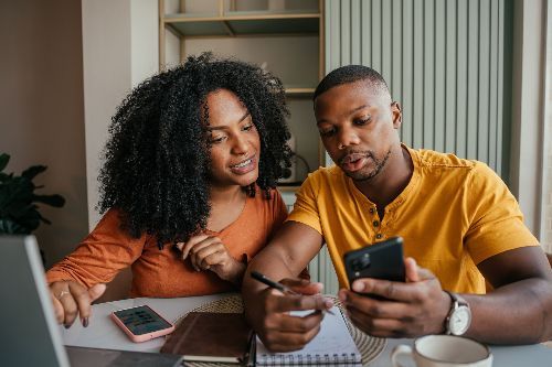 A man and a woman are sitting at a table looking at a cell phone.