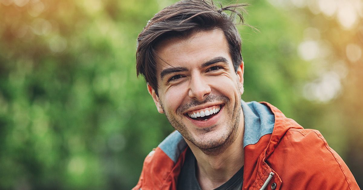 A man in an orange jacket is smiling for the camera.