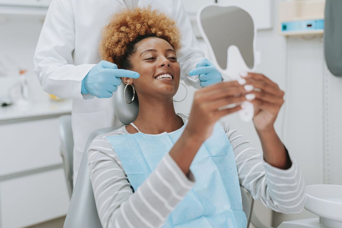 A woman is sitting in a dental chair looking at her teeth in a mirror.