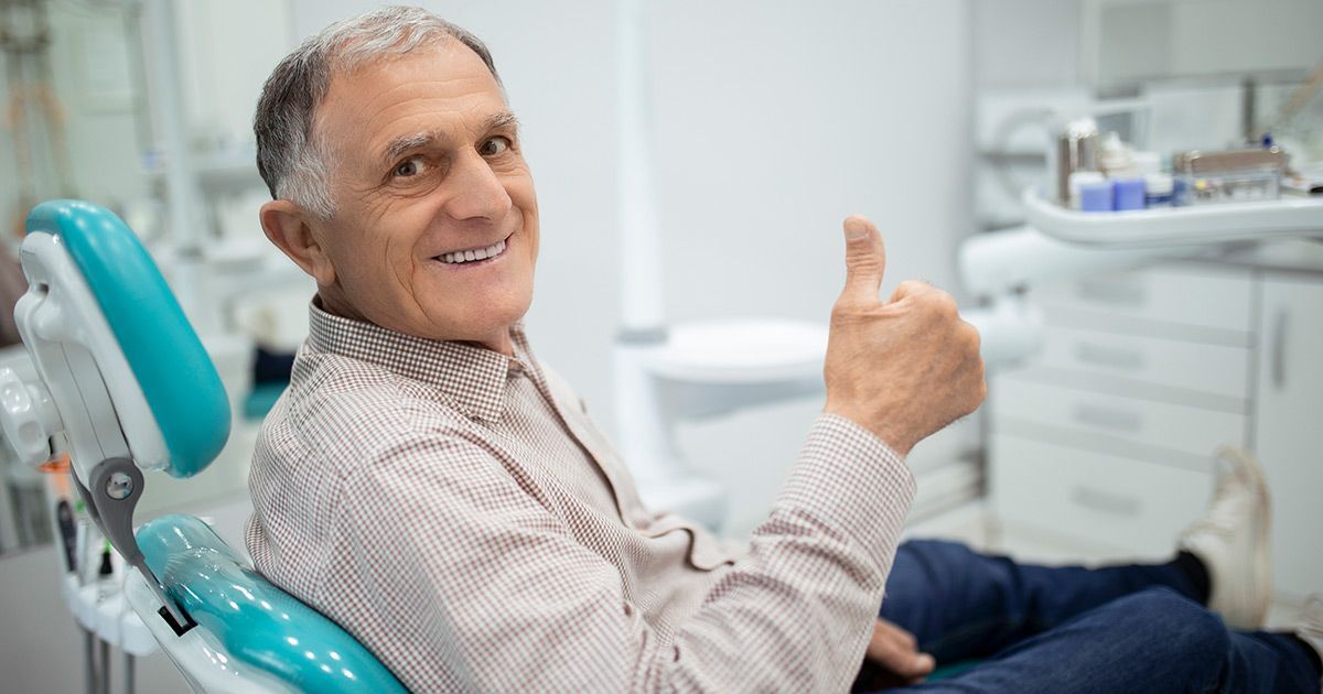 an elderly man is sitting in a dental chair and giving a thumbs up .