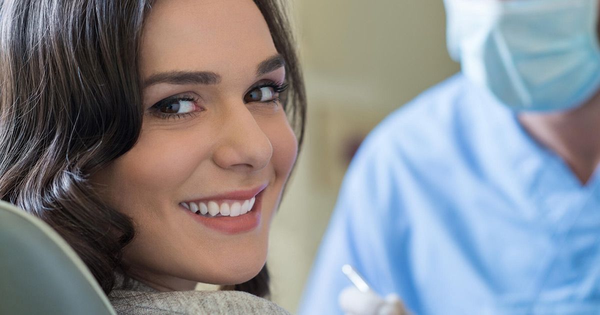 A woman is smiling while sitting in a dental chair.