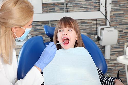 a little girl is sitting in a dental chair getting her teeth examined by a dentist .