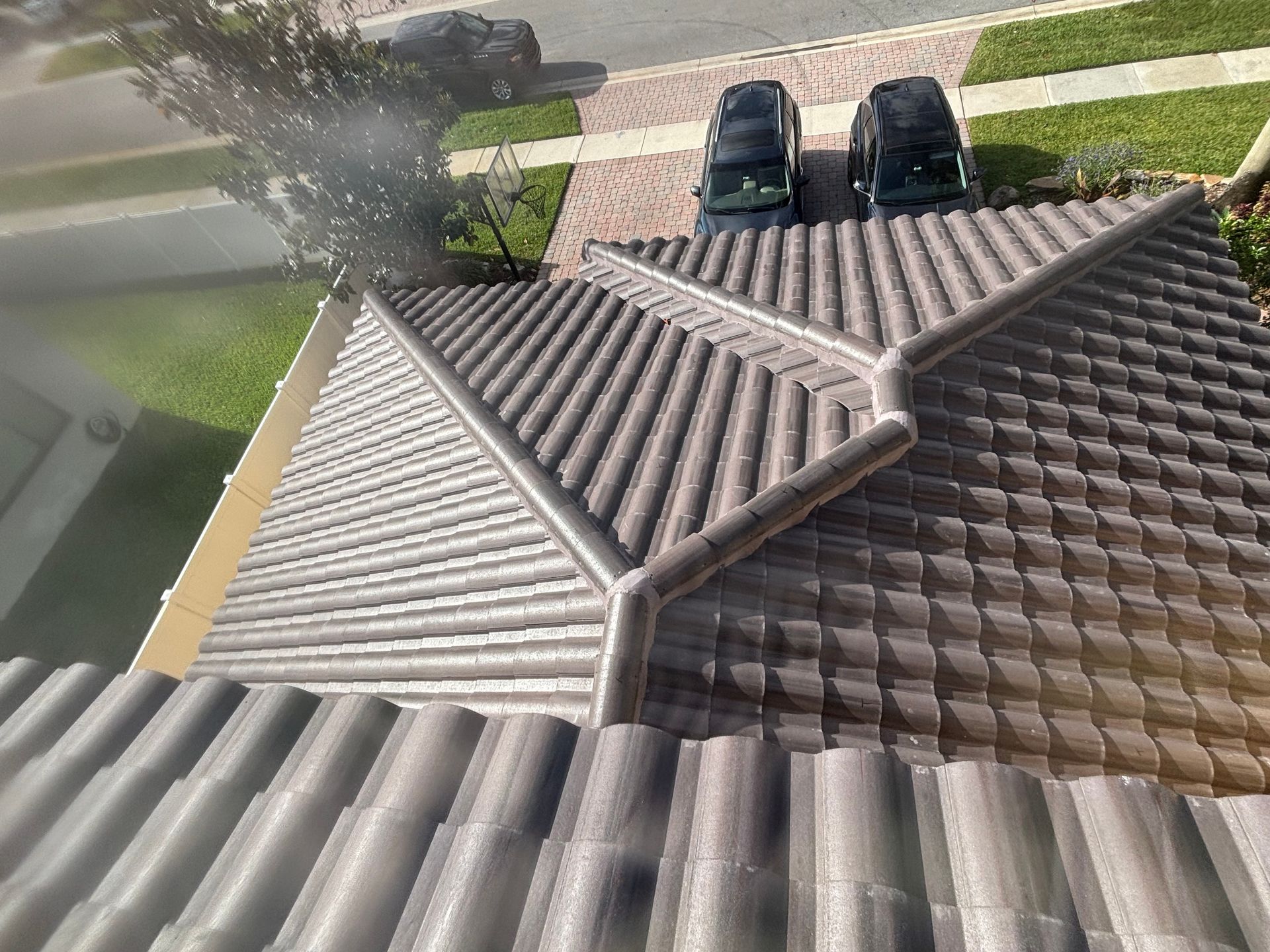 High-angle view of a brown tile roof with connected gutters, two black cars, and green grass.